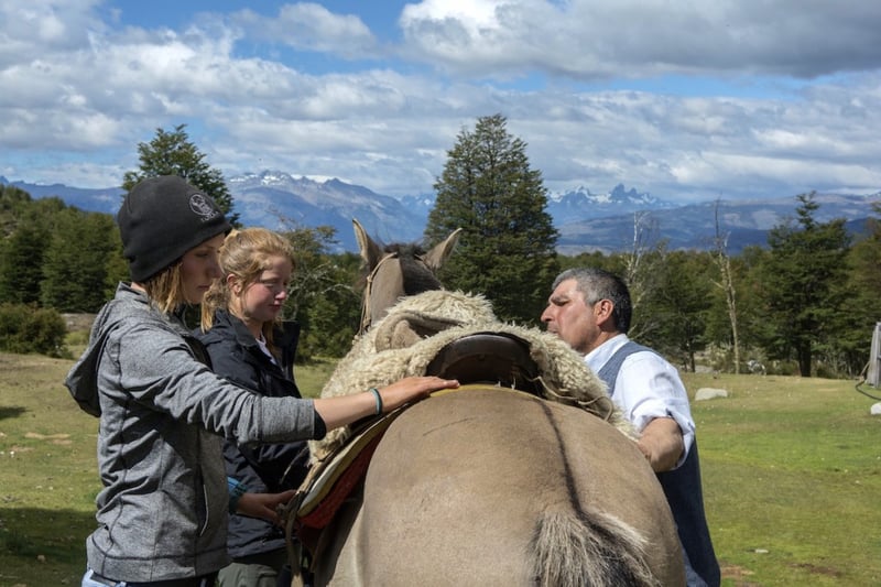 NOLS students learn how to put saddle on a horse with host family in Patagonia 