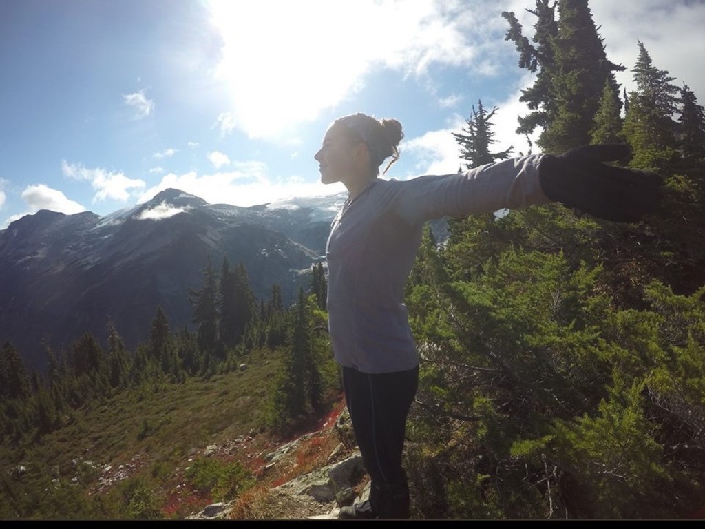 NOLS participant stretches her arms wide, enjoying sunshine in the mountains