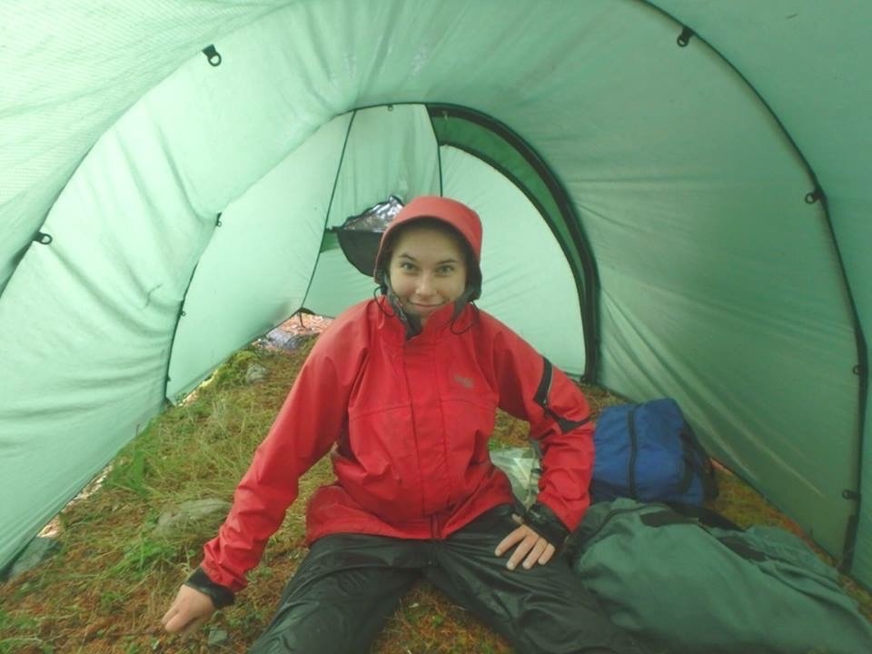 smiling NOLS student wearing rain gear sits in a tent