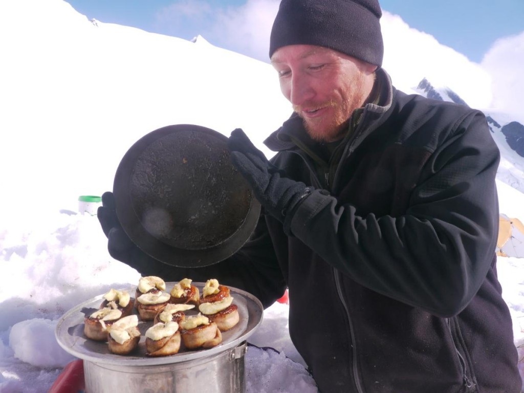 smiling NOLS participant takes the lid off a pan of hot buns