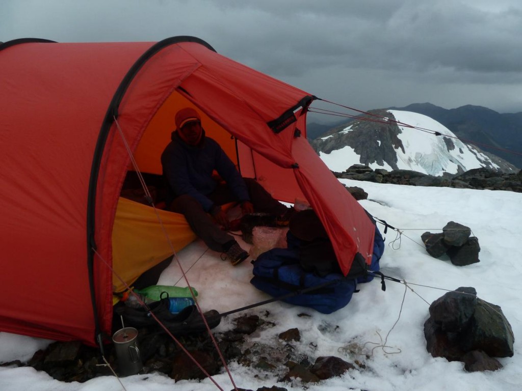 NOLS participant sits in the vestibule of tent in snowy mountains