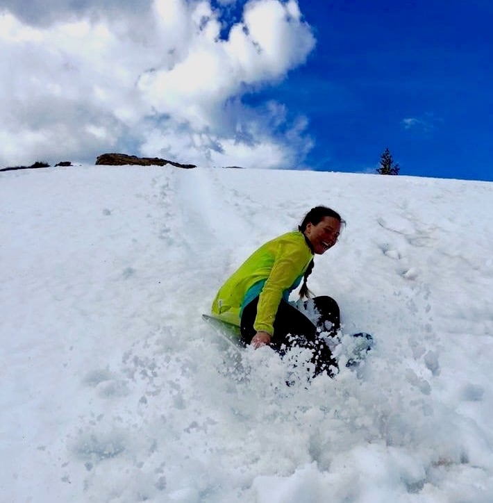 smiling person sleds down a hill in a spray of snow