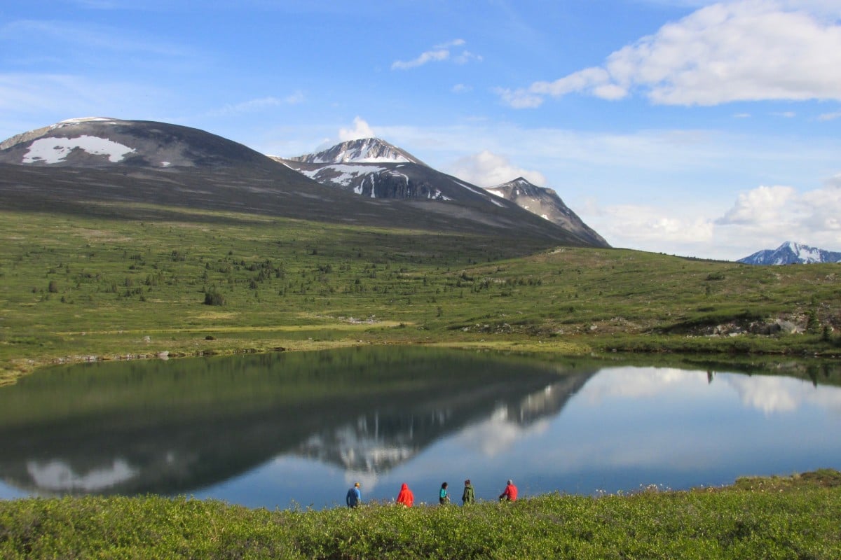 Group of people standing on a lakeshore with mountains in the background