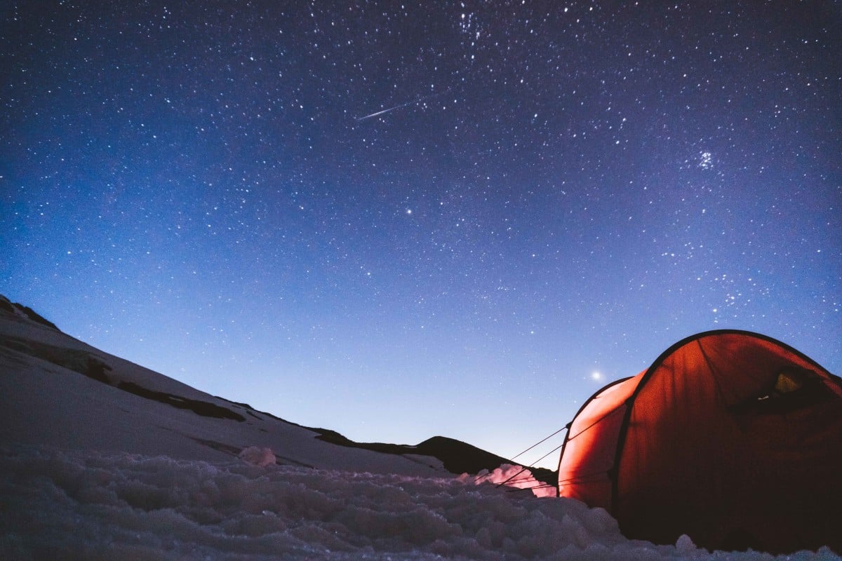 A tent at night in the snow with bright stars filling the sky