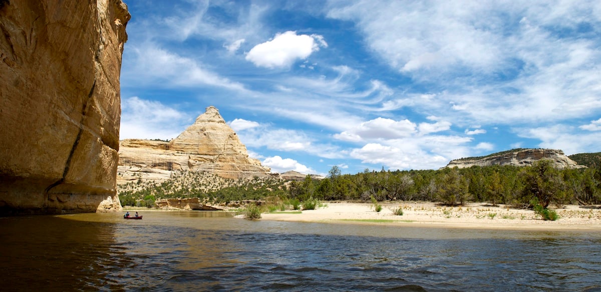 NOLS students paddle through Yampa Canyon on a sunny day with swirls of clouds above