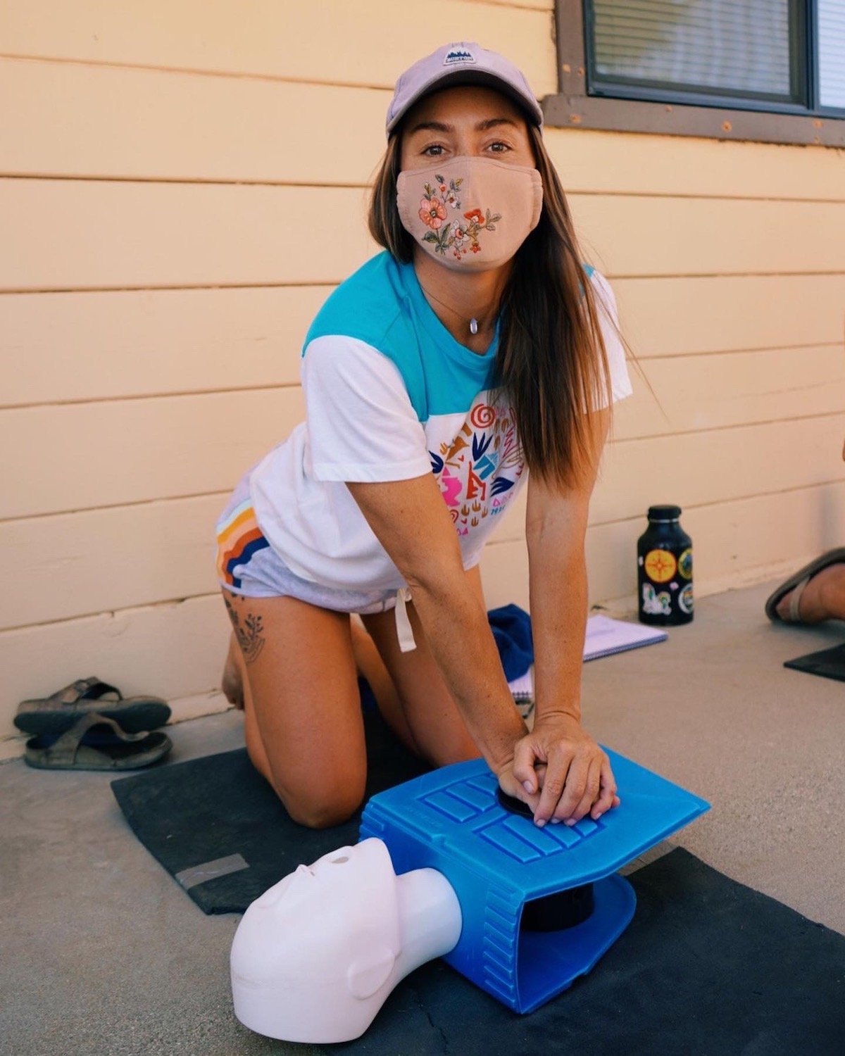 A woman in a face covering practices CPR on a plastic dummy