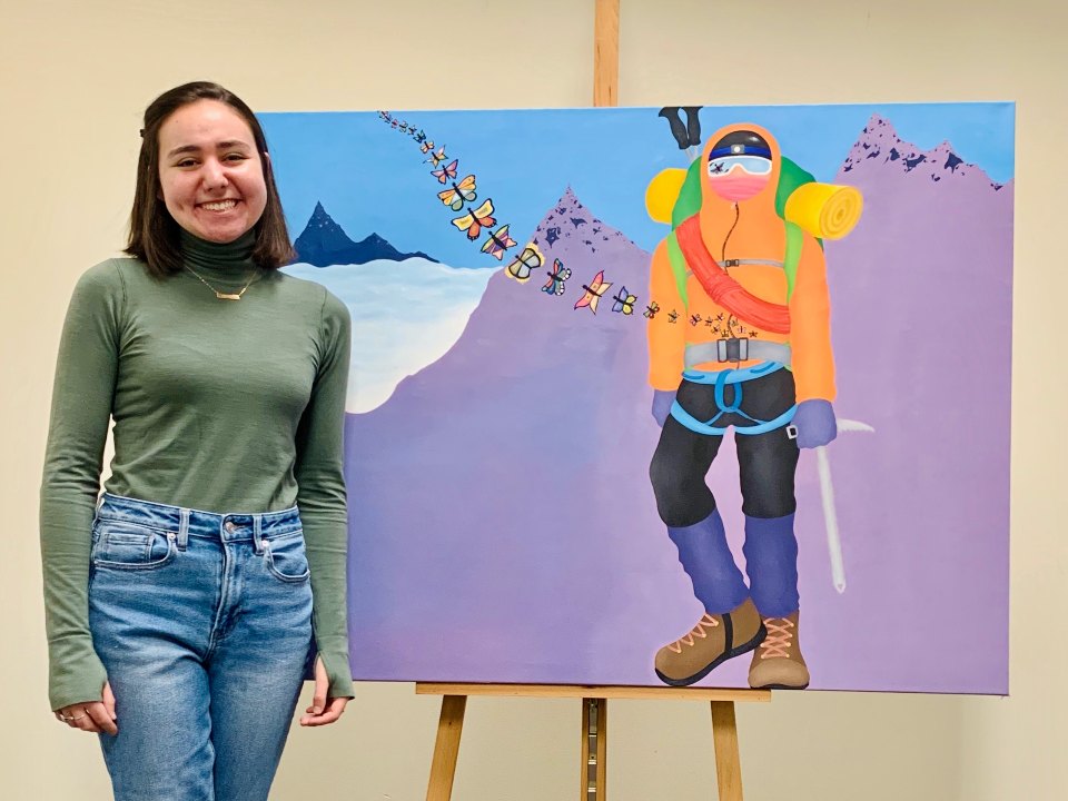 Artist smiles next to her painting of a mountaineer