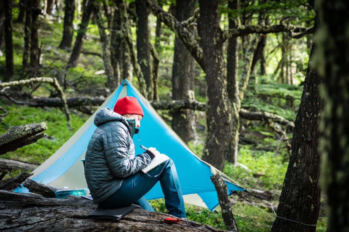 Man writes in a journal in front of his tent in the forest