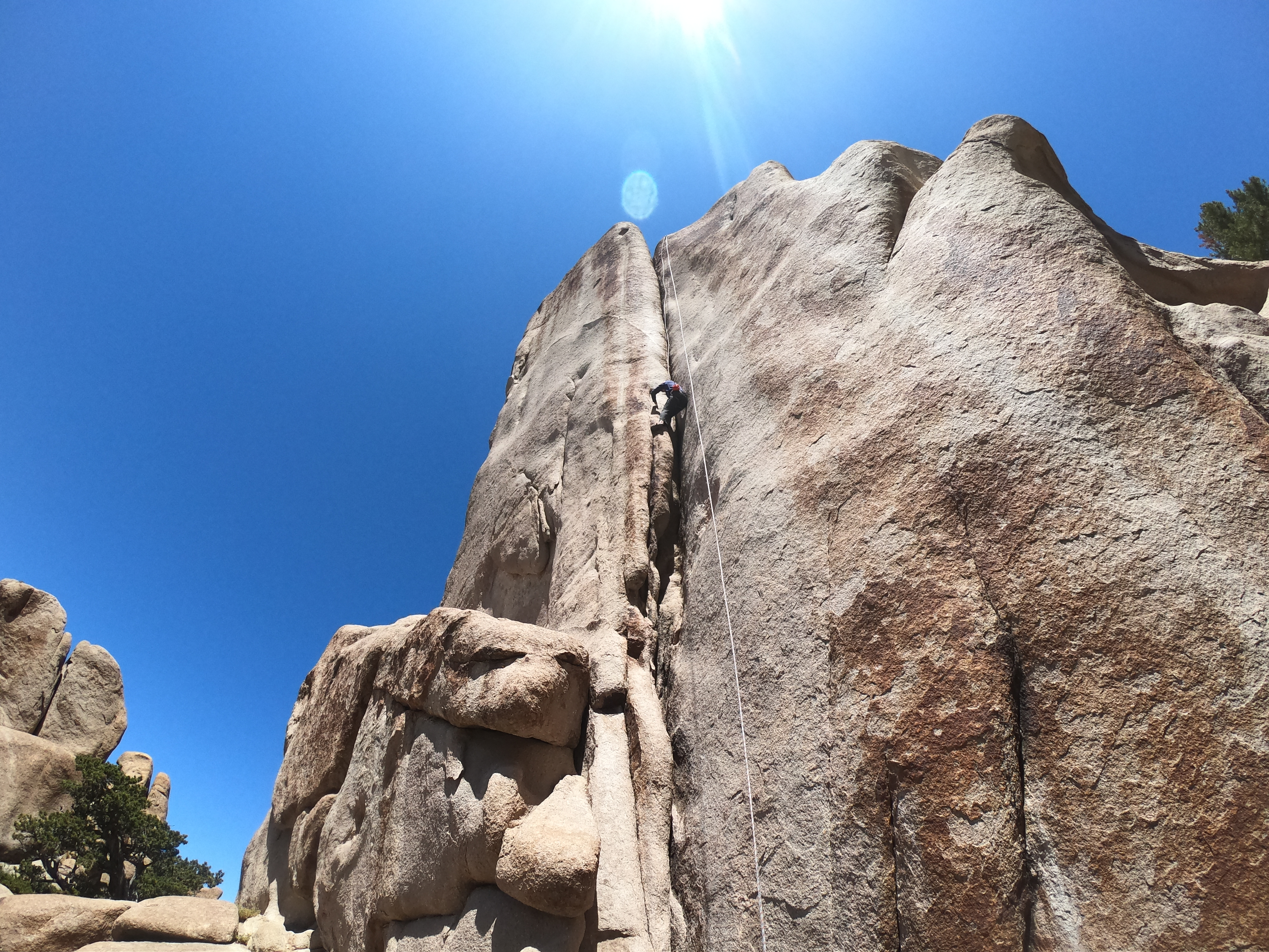 Student top-rope climbing a crack with blue sky and the sun above