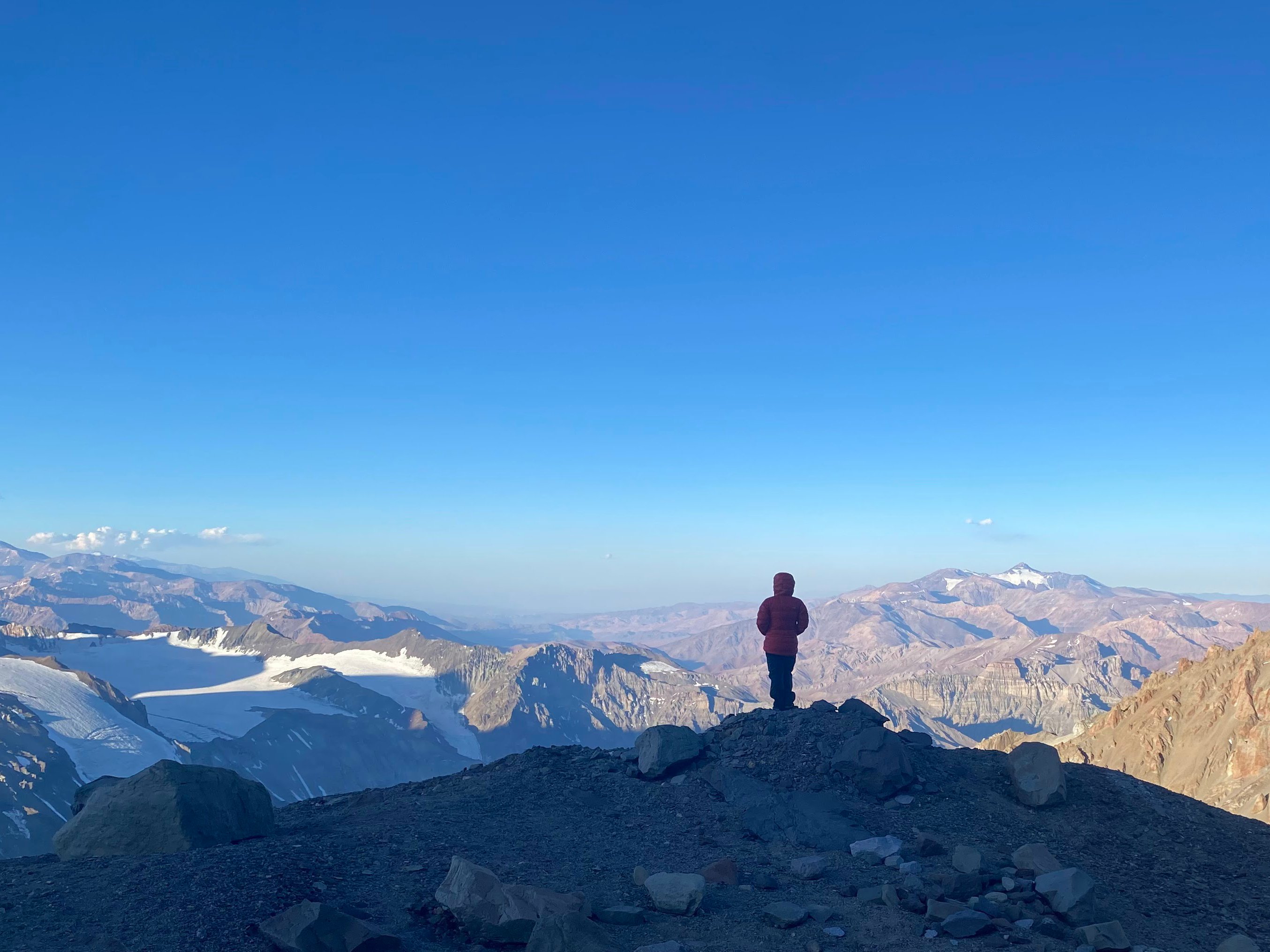 Solo person in a red parka looking out over a vast mountain range