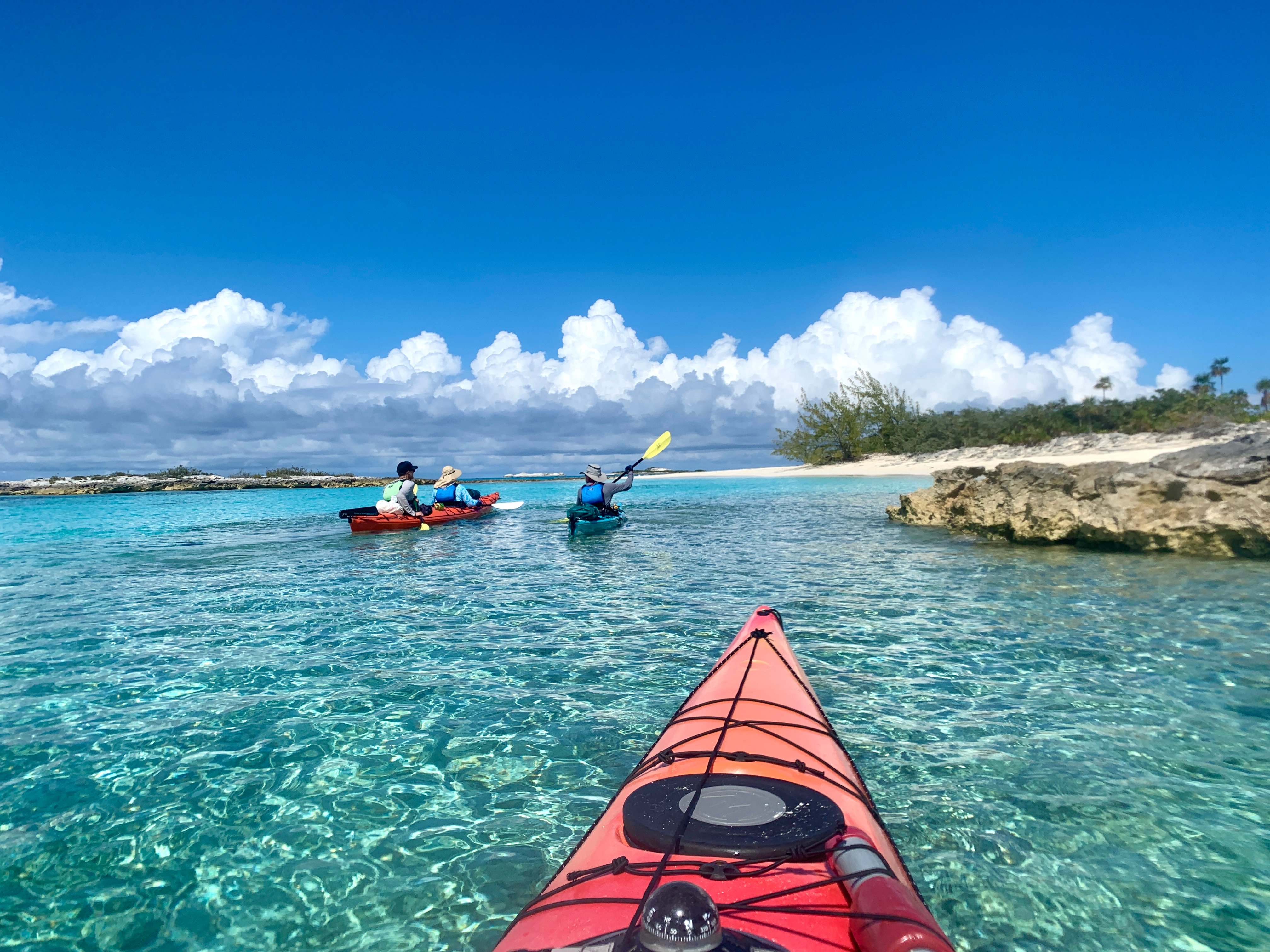 View from a kayak looking ahead to three other kayakers gliding over crystal clear water