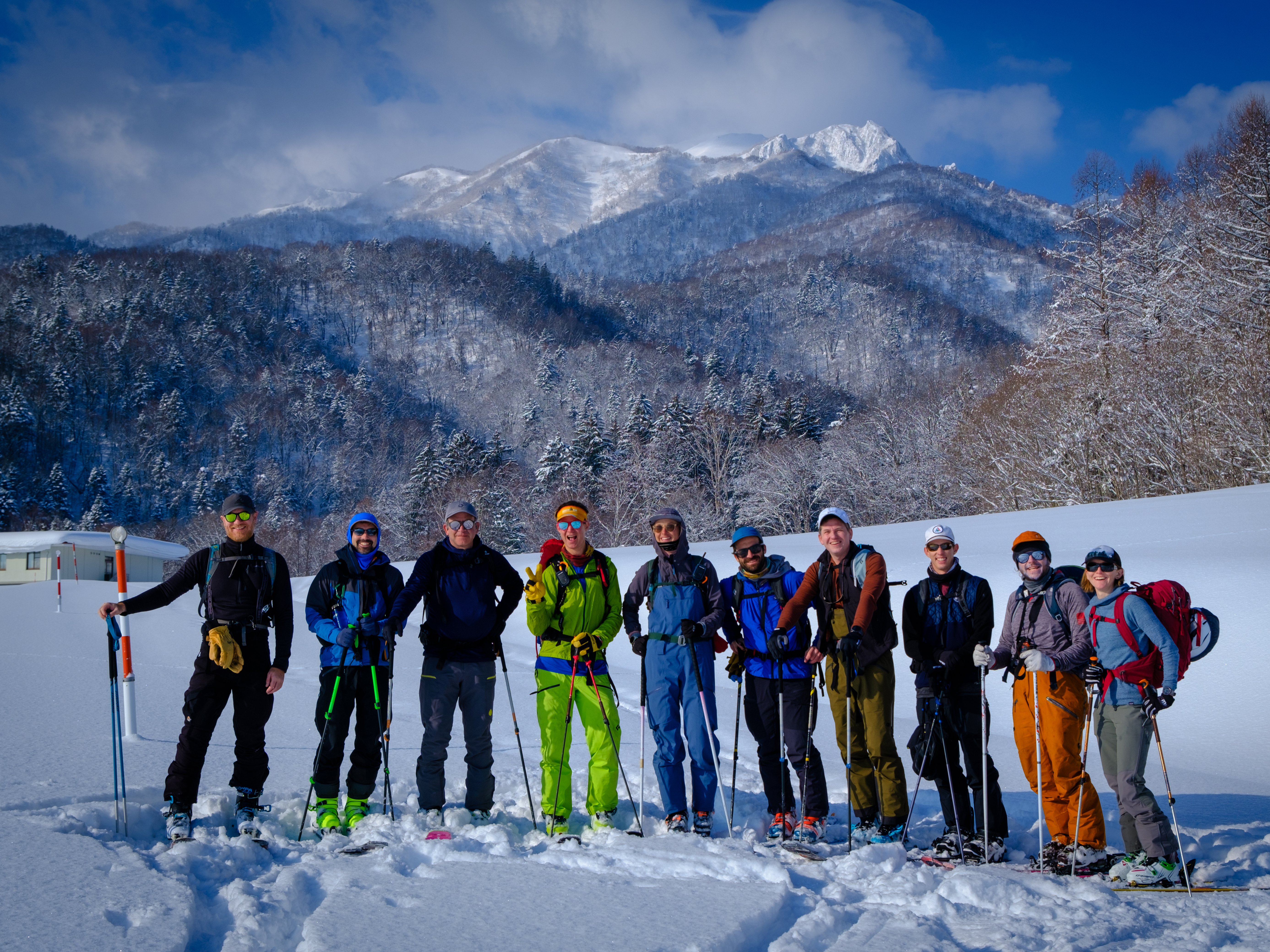 10 skiers gathered for a photo with tall snow-covered mountains in the background