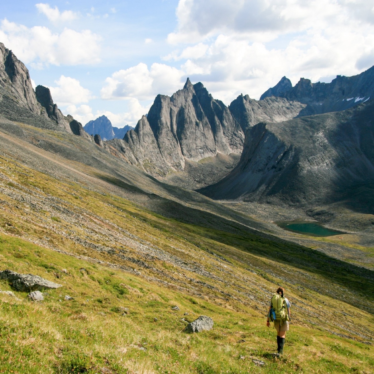 A hiker walks across the side of a valley with steep mountains in the background