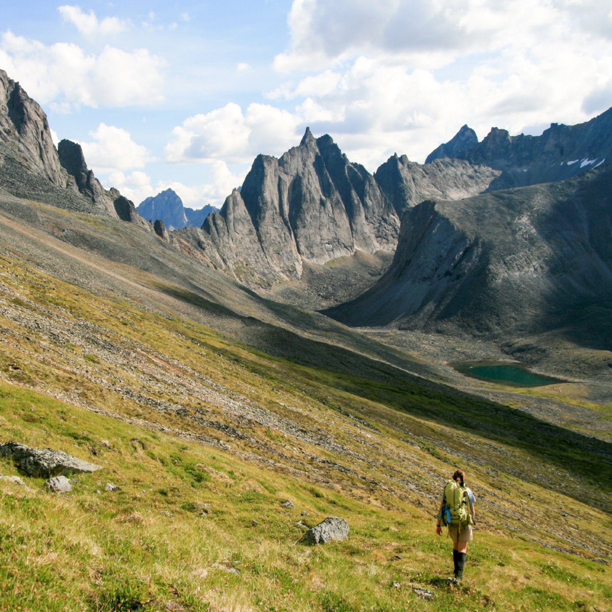 A hiker walks across the side of a valley with steep mountains in the background