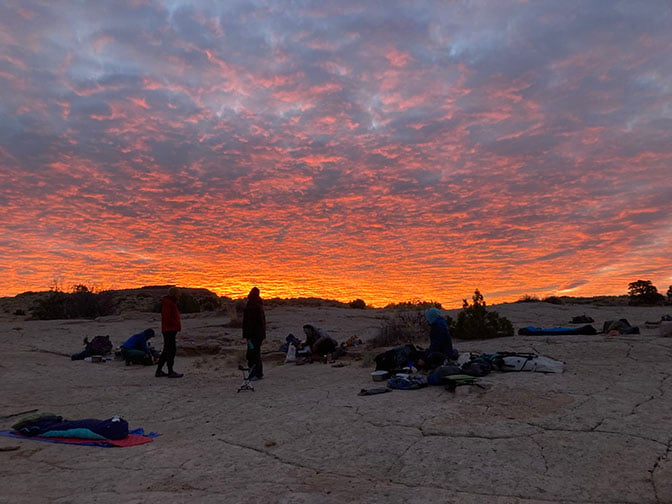 Students preparing camp at sunset with a golden light on the clouds