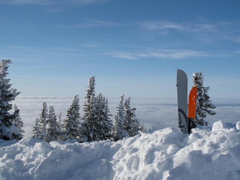 splitboard sticks out of a mound of snow in front of a sweeping view of mountains and clouds