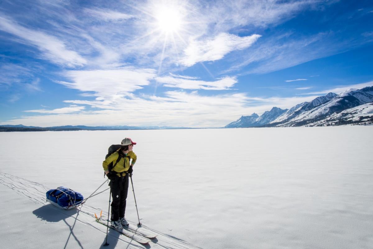 Person skiing and pulling sled pauses to look at Teton Mountains in the background