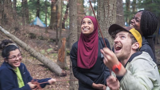 Students smile while pulling a rope that is attached to a tree. They are hanging a bag of food out of reach from bears