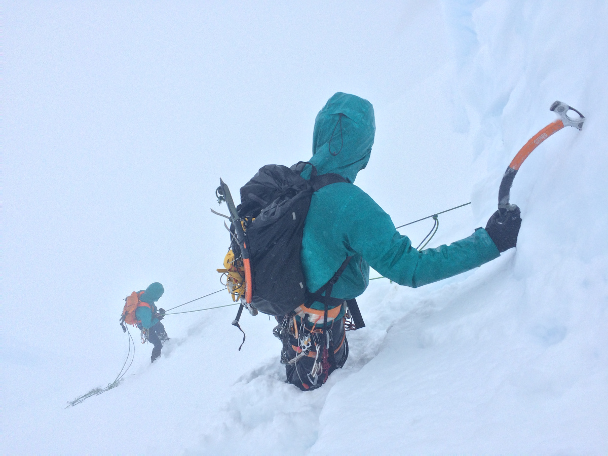 two climbers roped together use ice axes to ascend a steep snowy slope in a whiteout