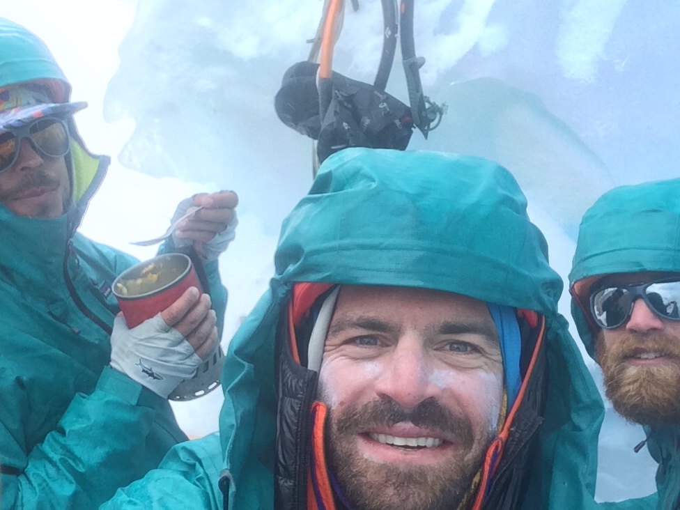 three men in turquoise jackets smile for the camera while mountaineering in Patagonia