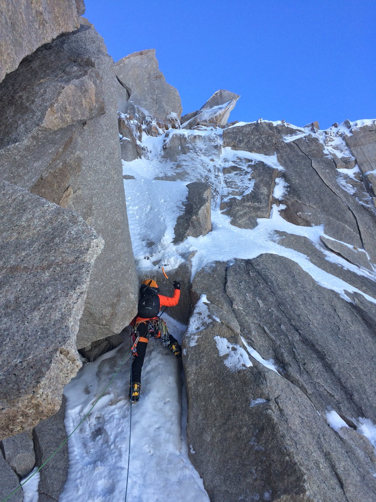 mountaineer in a climbing harness uses ice axe to ascent snow and rock in Patagonia