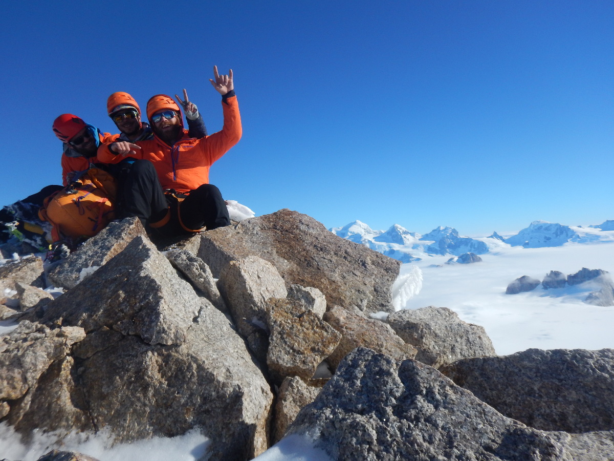 three mountaineers in orange jackets and helmets sit on a rock outcropping at Pantagruel's summit