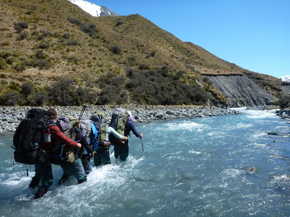 Group of four backpackers crosses a river in a line