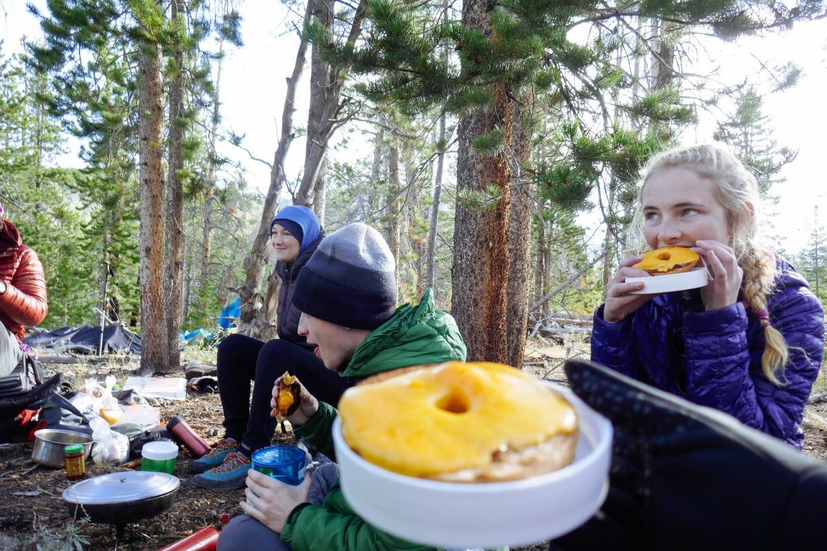 Teen eats a cheese covered bagel at a campsite