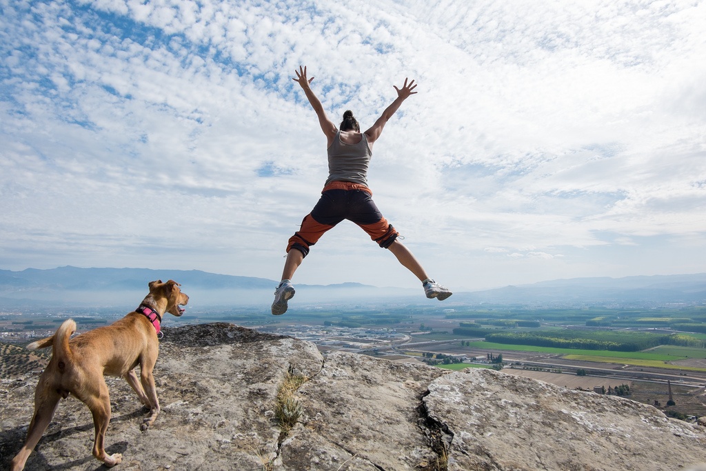 Person jumps happily while a dog watches