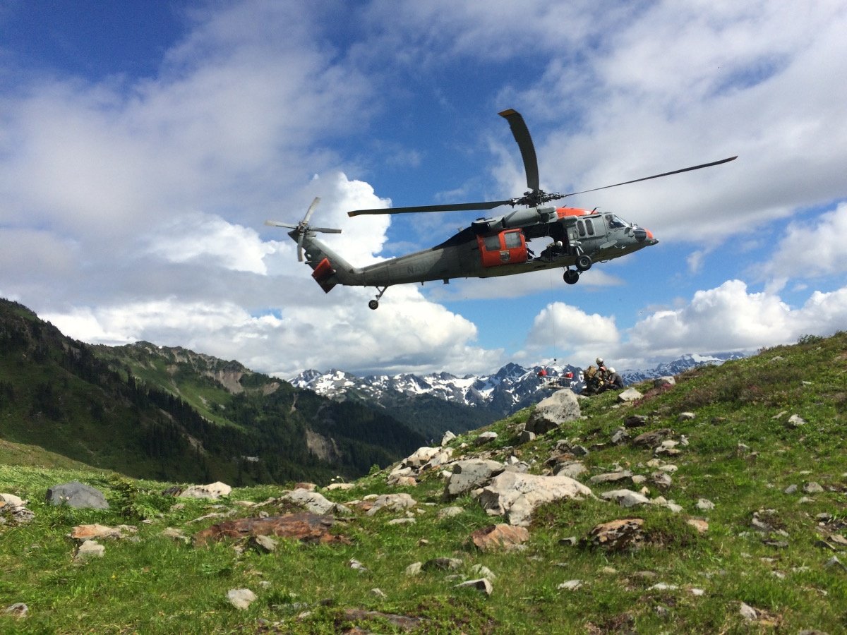 A rescue helicopter flies over a rocky mountain meadow