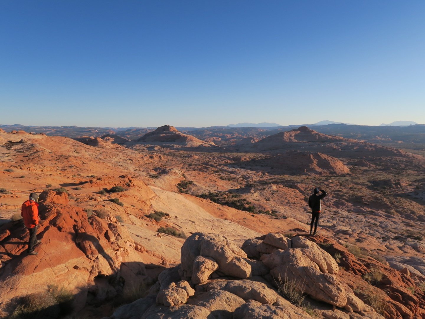 two people stand on red rock formation in the Southwest, gazing out at the landscape