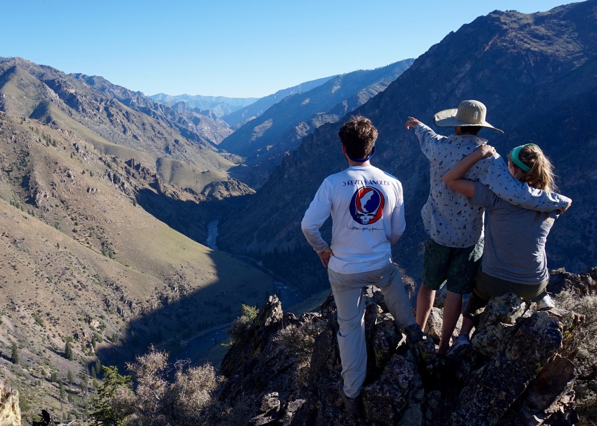 three family members stand with their backs to the camera and look out at the mountains