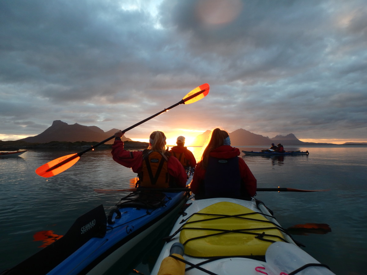 group of kayakers paddling at sunset in Scandinavia with one person holding a paddle aloft
