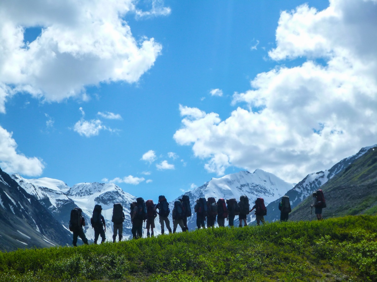 large group of backpackers standing on grass looking toward snow-capped peaks and facing away from the photographer
