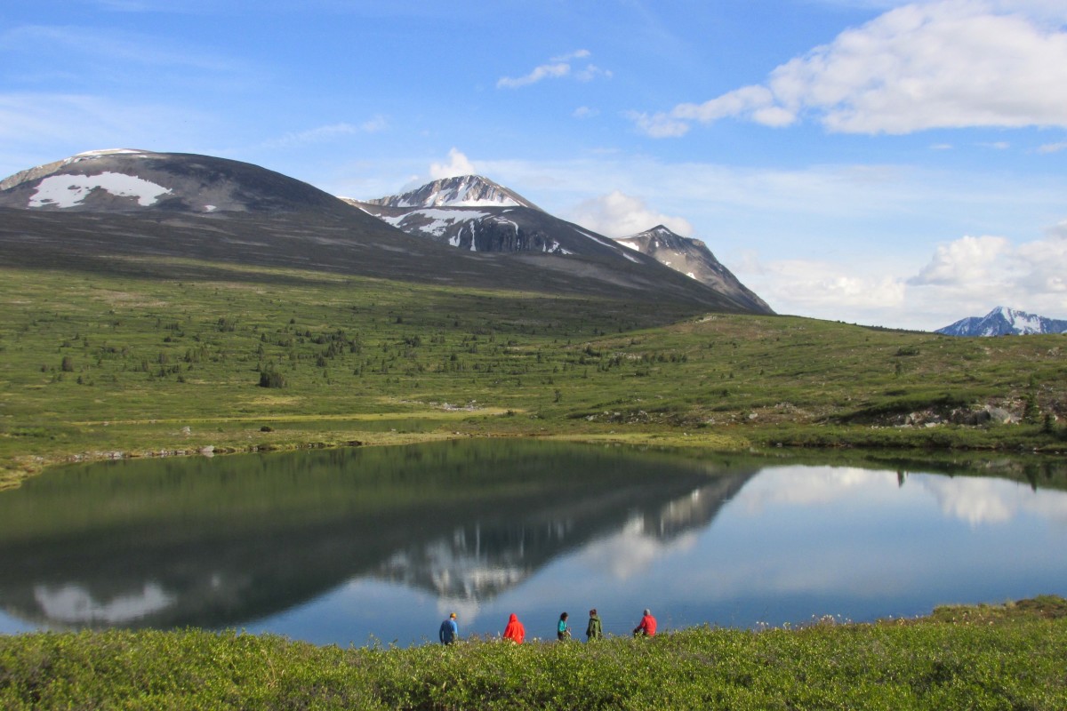 Five NOLS participants on the edge of a glassy lake reflecting the landscape in the Yukon's Coast Mountains