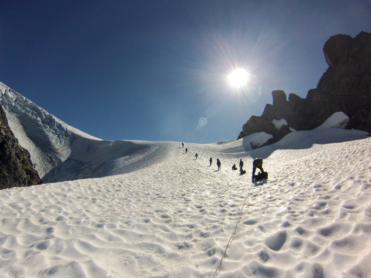 distant figures on a rope team climb a steep snowy slope while mountaineering in the Pacific Northwest