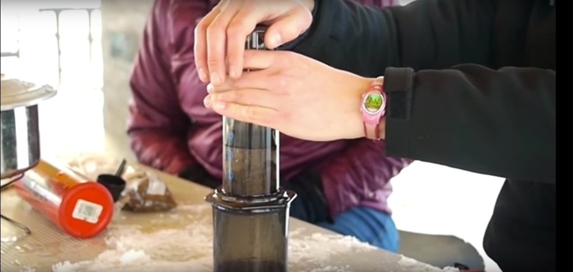 hands using an aero press sitting on a table to make coffee