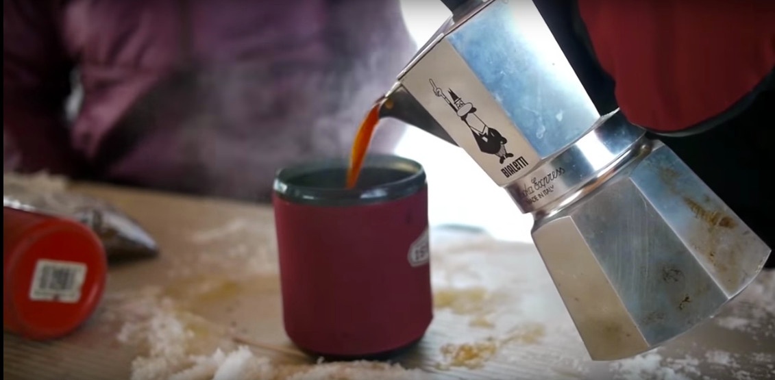 Pouring coffee into a red mug from metal bialetti