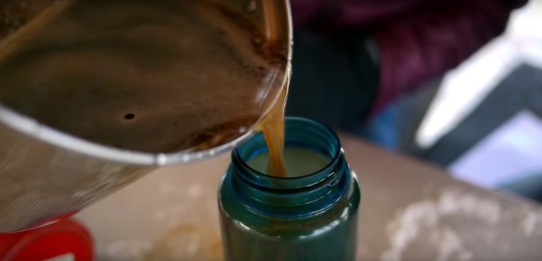 pouring coffee from a metal container into a blue plastic bottle