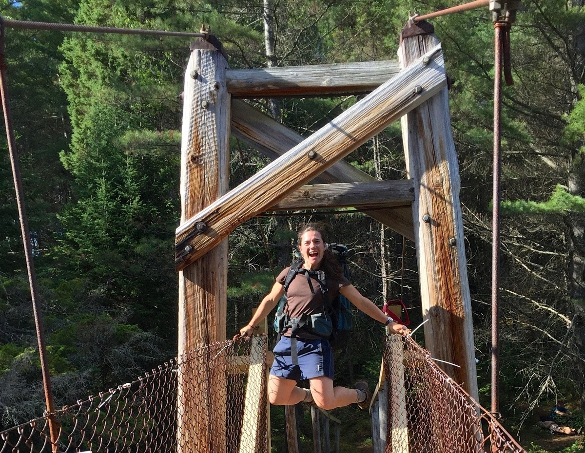 Smiling woman jumps in the air at the end of a wooden bridge she helped build