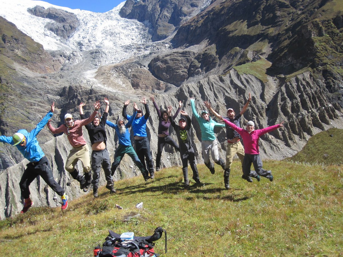 Smiling NOLS students and instructors leap into the air in the mountains on a sunny day in India