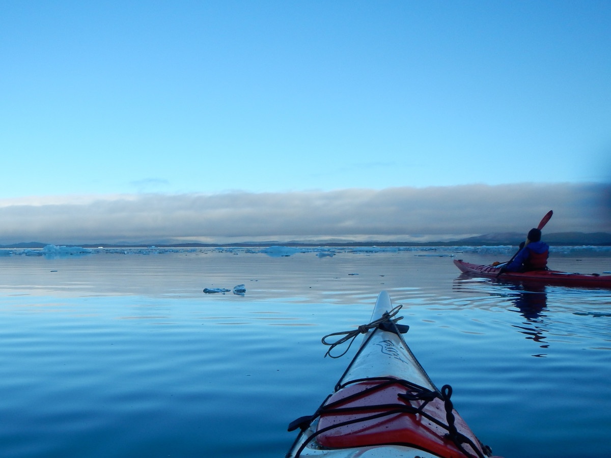 kayaker paddling smooth blue water in Patagonia, as seen over the nose of photographer's kayak