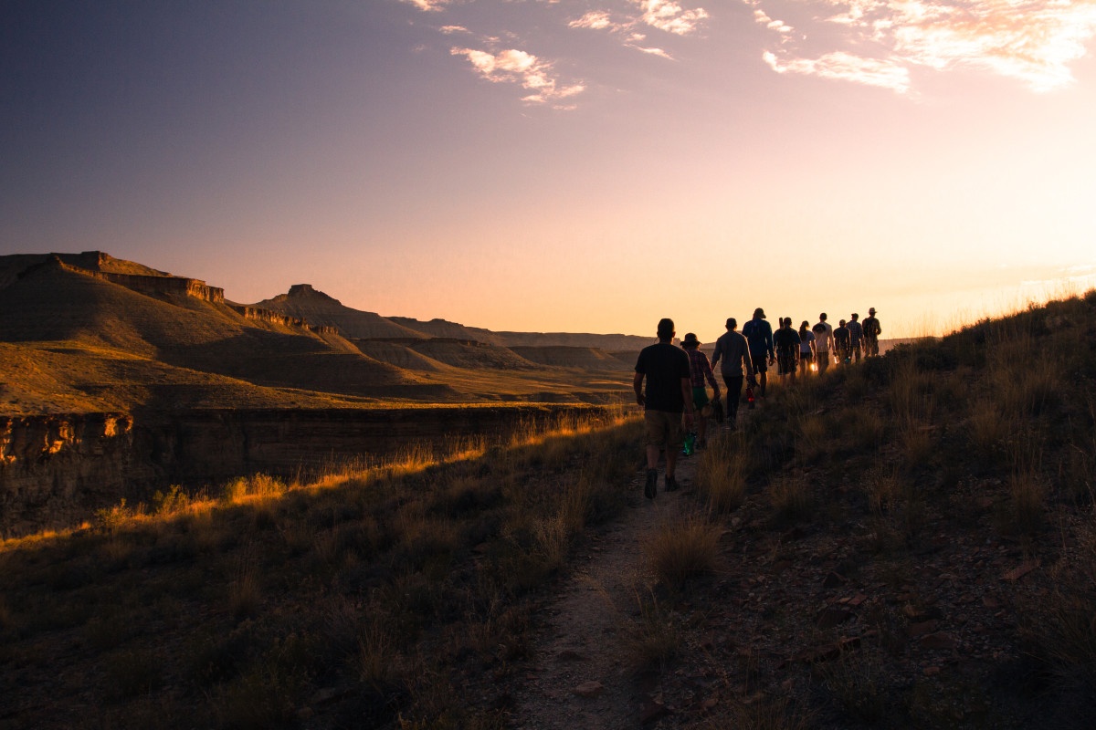 students hike in a line along a trail on a river course as the sun sets