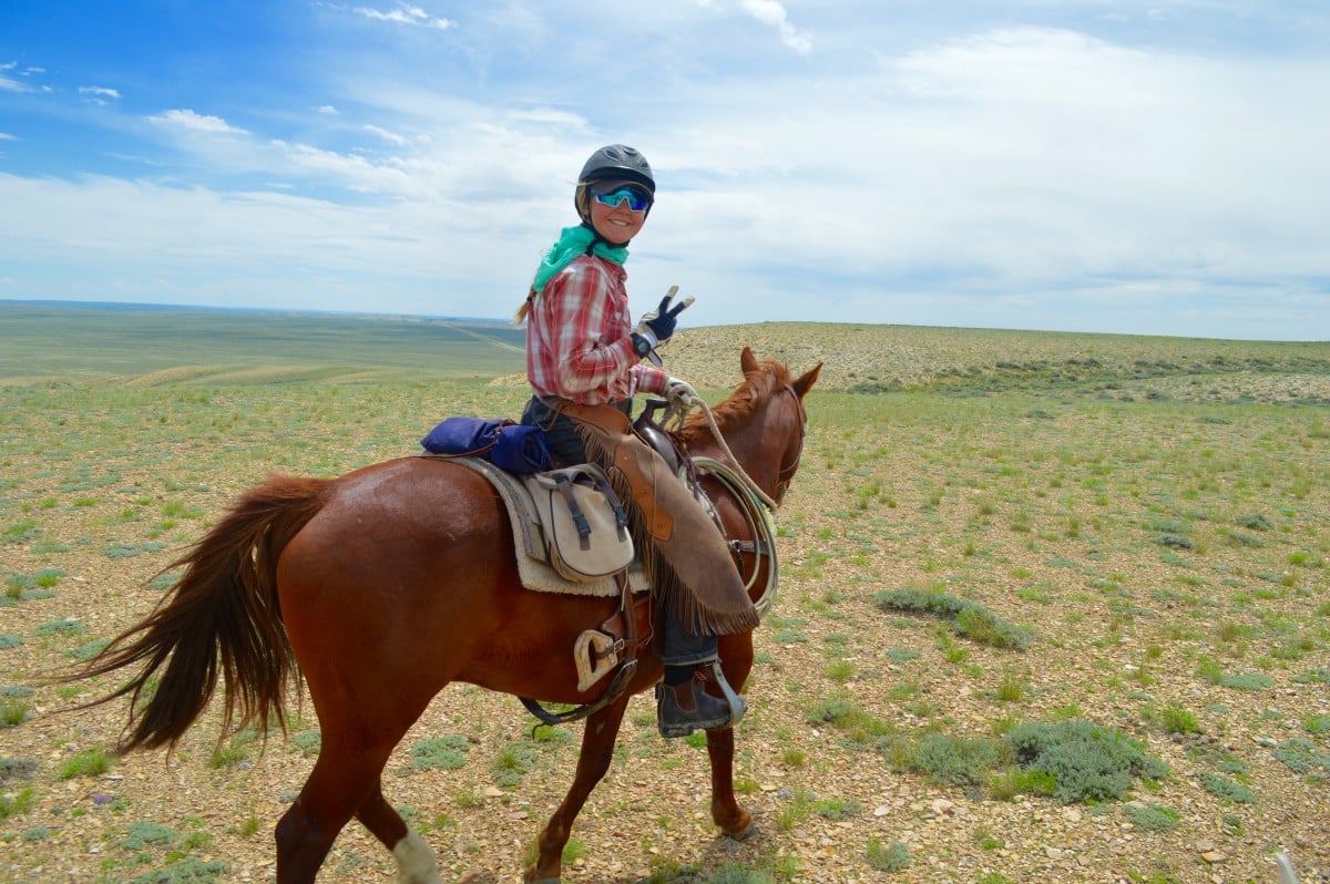 smiling student on horseback wearing Western attire looks back over her shoulder