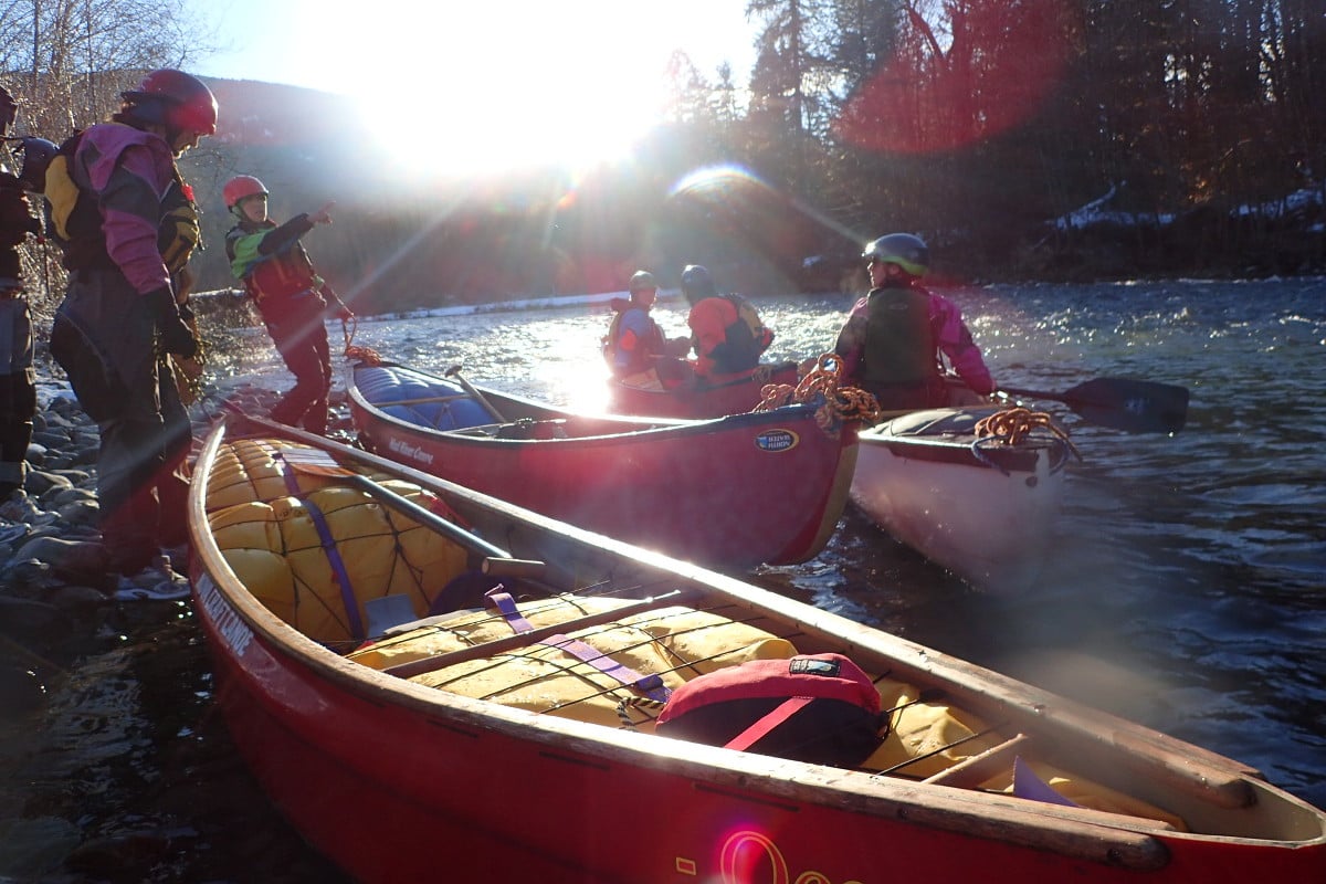 Paddlers on the edge of a river in the morning, getting canoes and equipment ready for the day
