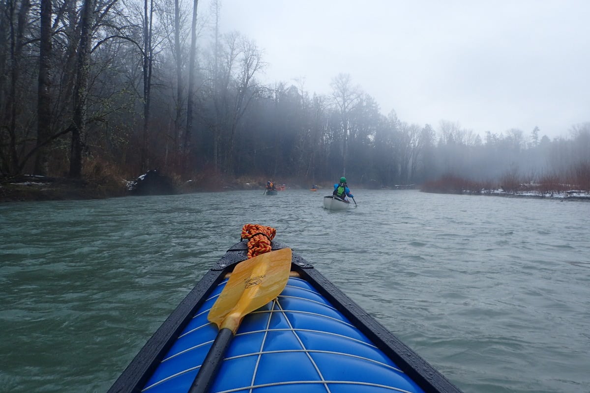 Looking over the bow of a canoe on a quiet section of river with other paddlers up ahead