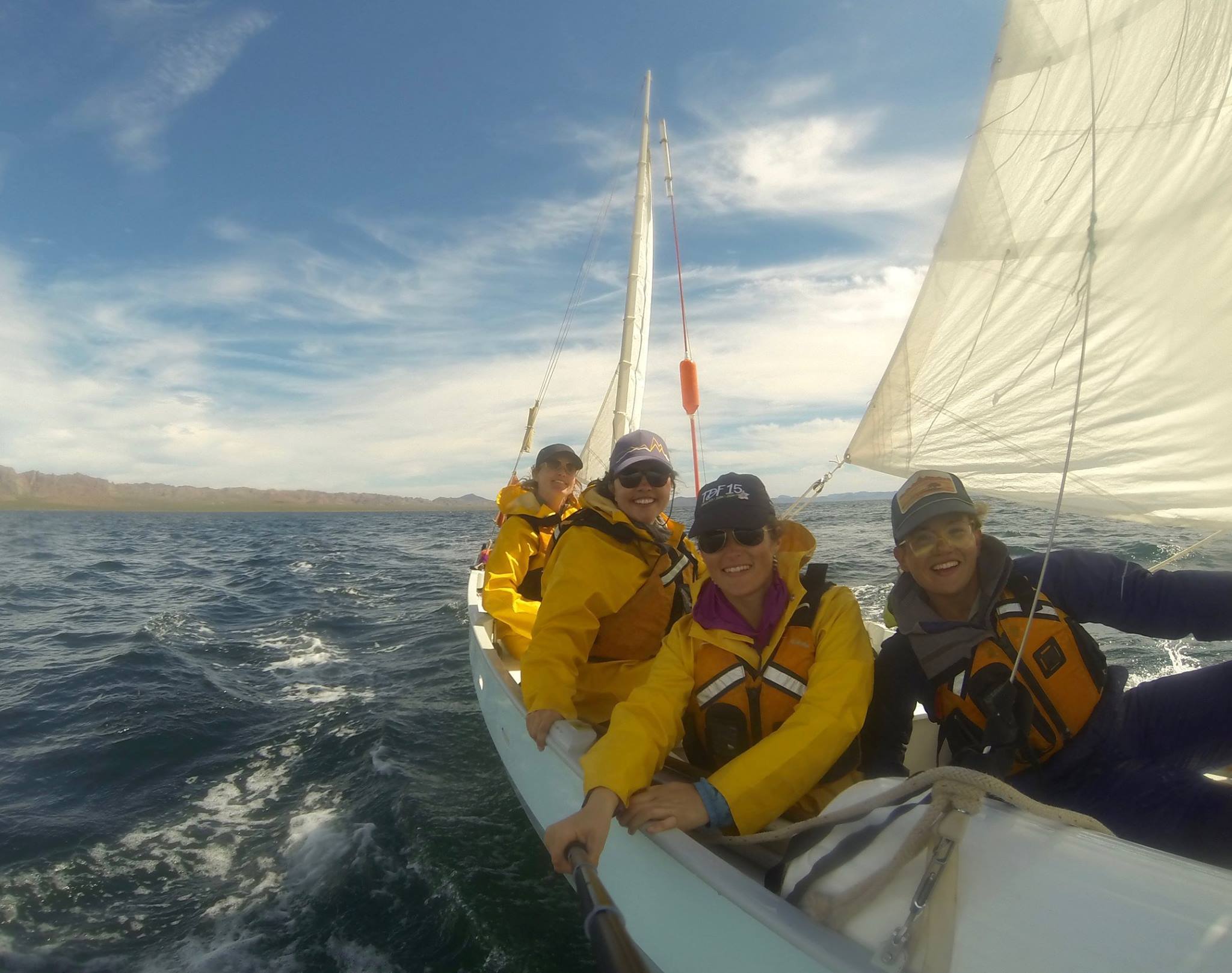 four smiling people wearing life preservers sailing a Drascombe Longboat in Baja