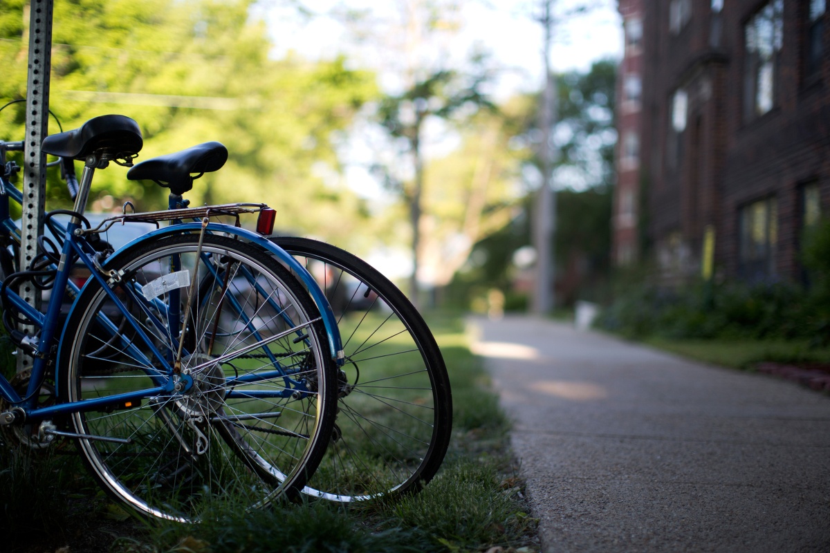 two bikes locked to a metal post in the grass near a sidewalk