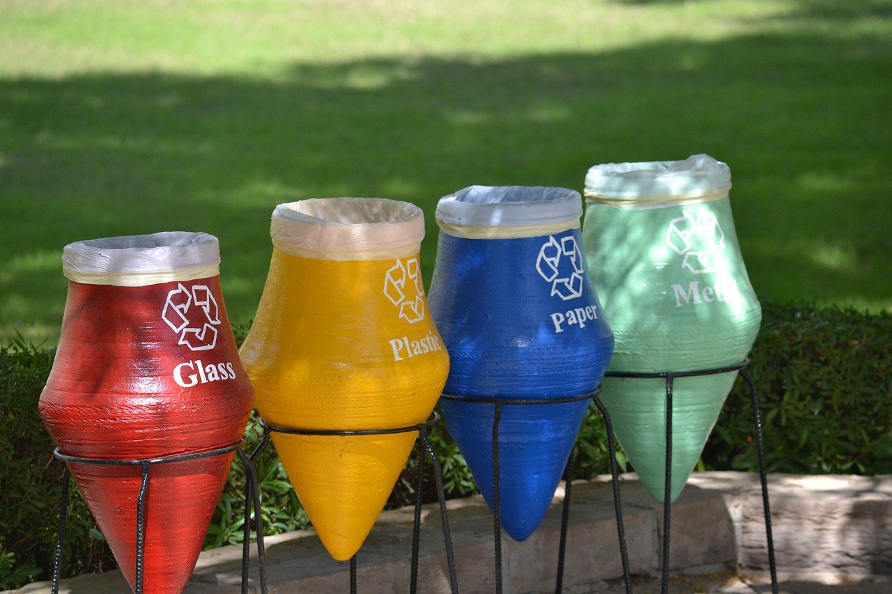 four brightly colored recycling containers shaped like crayon tips for glass, plastic, paper, and metal items