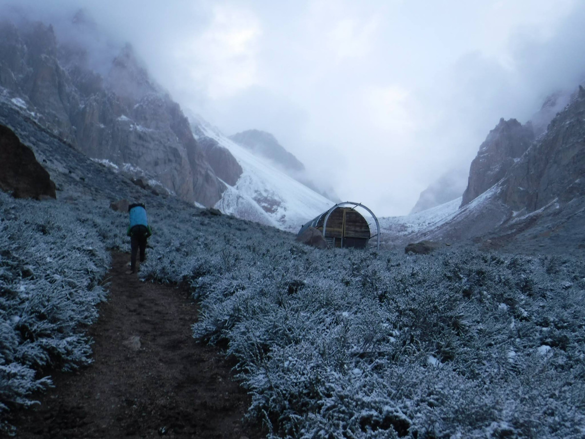 person walking down dirt path with snowy vegetation on either side and a tent to the right